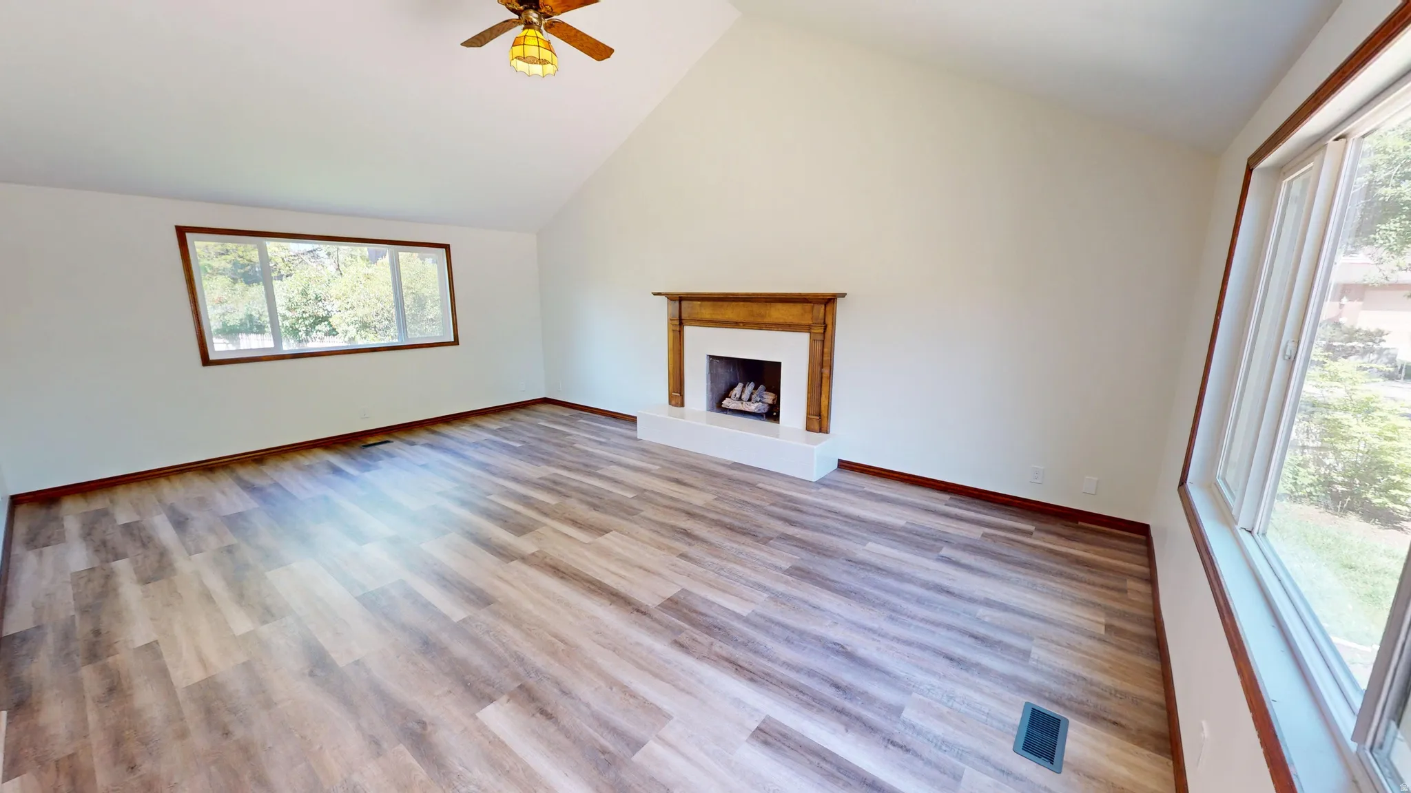 Spacious room featuring wood-finish flooring, a vaulted ceiling, a ceiling fan, and multiple windows