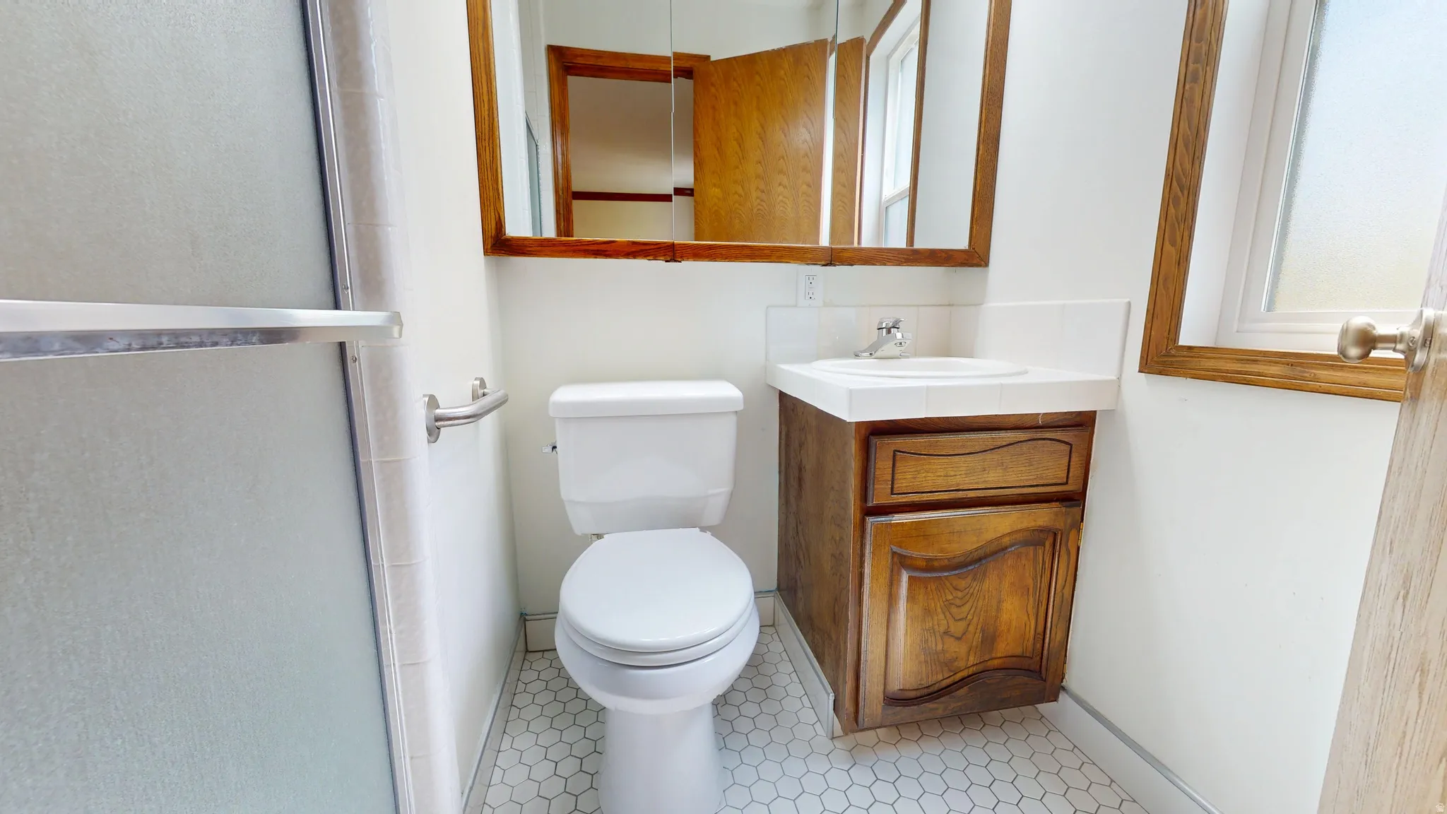 Bathroom featuring hexagonal floor tiles, a white toilet, and a wood-finish vanity with a white countertop and integrated sink