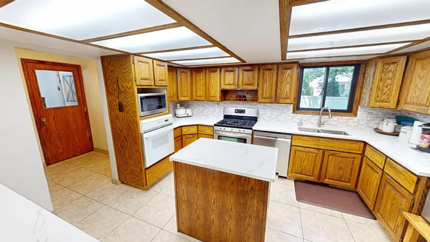 Kitchen featuring wood cabinetry, white countertops, tile flooring, a built-in oven, and a center island