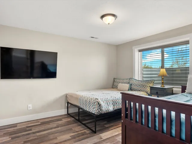 Bedroom featuring wood-finish plank flooring, a wall-mounted television, and a window with blinds
