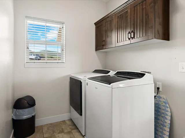 Laundry space featuring upper wood cabinetry, tiled flooring, and a window with blinds