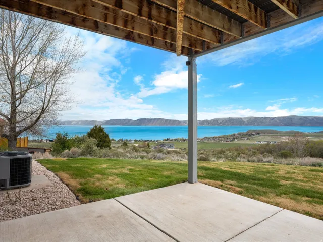 Covered concrete patio with expansive water and mountain scenery, featuring a grassy yard and structural support beams