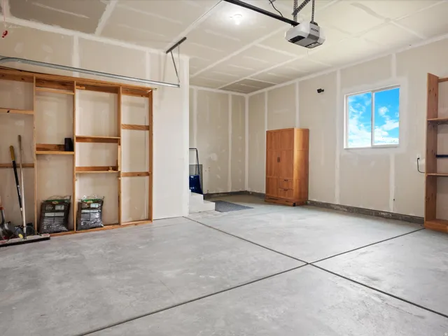 Spacious garage featuring a concrete floor, built-in wooden shelving, and a large window providing natural illumination