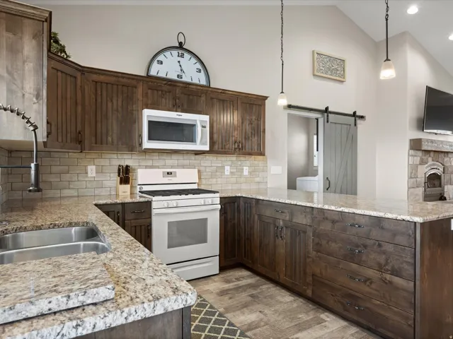 Kitchen featuring wood-finish cabinetry, light-toned countertops, subway tile backsplash, stainless steel double basin sink, and a barn door entry to an additional space