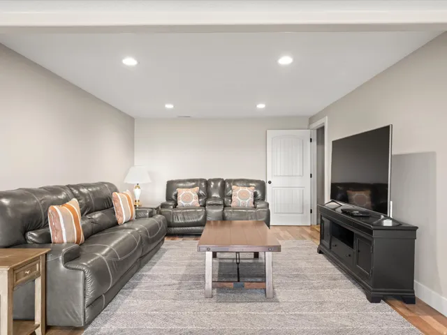 Recessed lighting illuminates this living space featuring light neutral wall paint, wood-finish flooring, a textured area rug, and a white paneled door
