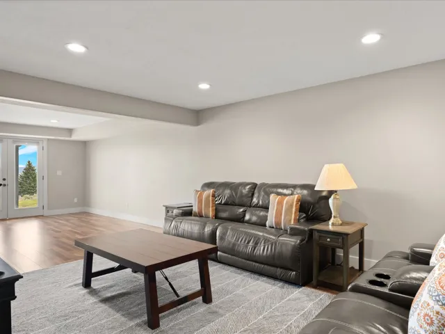 Spacious open-concept room featuring light-toned walls, recessed lighting, and wood-finish flooring extending to white French doors