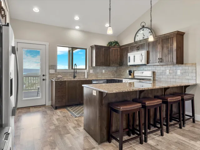 Spacious kitchen featuring an expansive island with seating, wood-finish flooring, wood cabinetry, a tile backsplash, and a glass-paneled exterior door