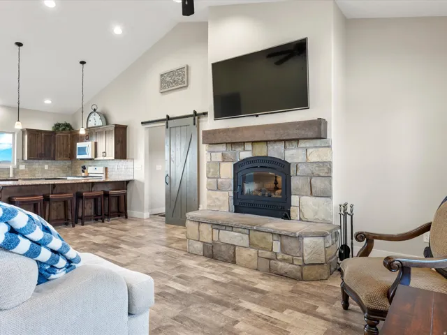 Open-concept living space with vaulted ceilings, featuring a stone fireplace with a wood-finish mantle and hearth
