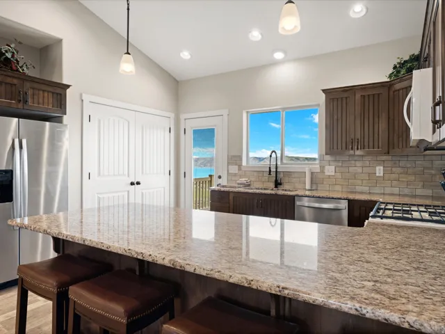 Spacious kitchen featuring a large island with a stone-finish countertop, stainless steel appliances, dark wood cabinetry, and a subway tile backsplash
