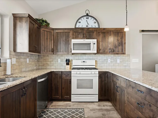 U-shaped kitchen featuring wood-finish cabinetry with black hardware, light-toned granite countertops, and a subway tile backsplash