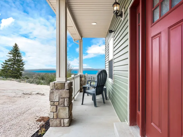 Inviting front porch featuring a red panel door with upper glass inserts, light green horizontal siding, and a stone-clad column base