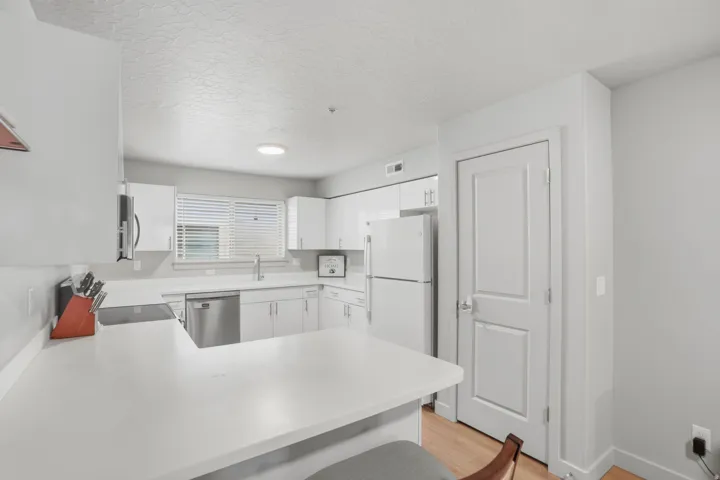 Modern kitchen featuring white cabinetry, light countertops, a stainless steel dishwasher, a built-in cooktop, and a white refrigerator