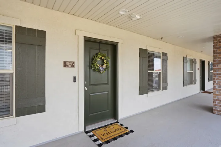 Inviting entry featuring a paneled door with white trim, stucco exterior, and decorative shutters