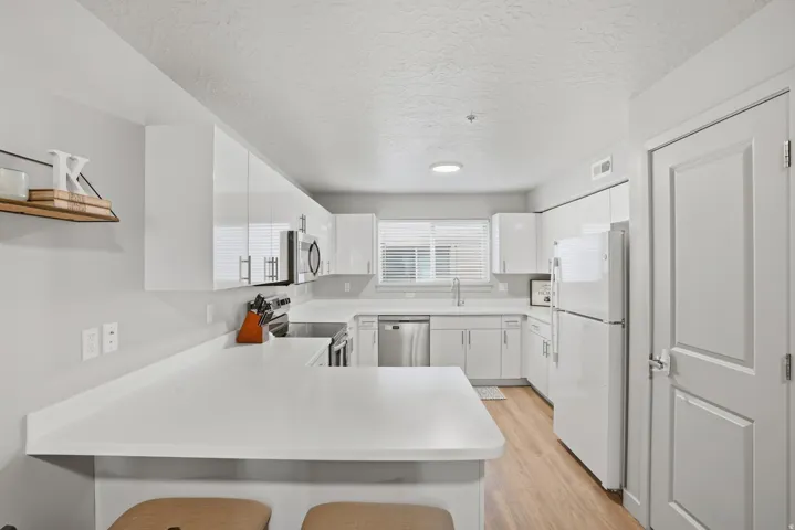 Modern kitchen featuring white cabinetry, light countertops, stainless steel appliances, wood-finish flooring, and a breakfast bar