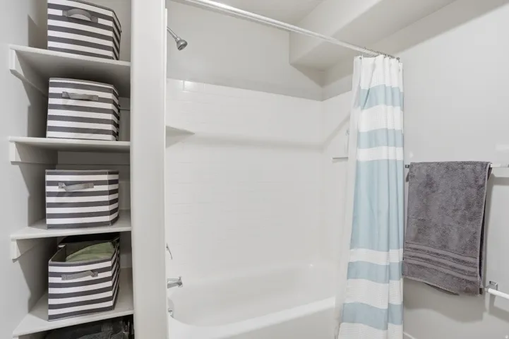Alcove bathtub with white subway tile surround, chrome fixtures, and built-in shelving