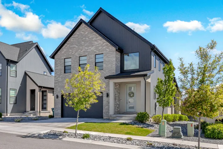 Modern two-story residence featuring a brick and stucco exterior, a dark-toned garage door, and a covered entry