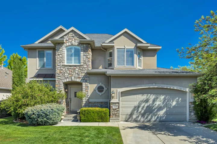 Two-story stucco and stone exterior featuring an arched entryway, an integrated two-car garage, and established landscaping