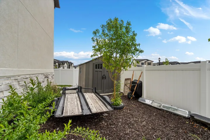 Rear yard featuring a white vinyl fence, established tree, and a storage shed