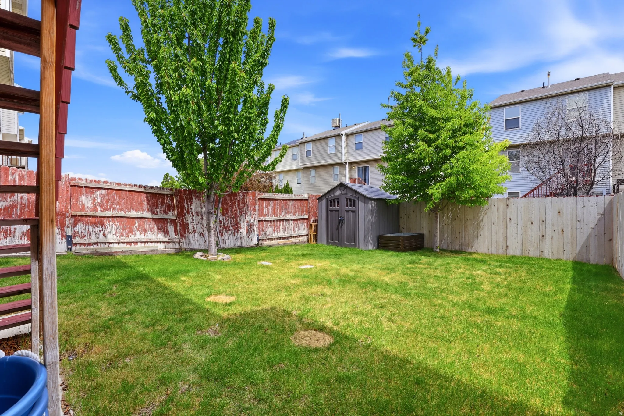 Expansive grass lawn with mature trees and a storage shed, bordered by wood fencing