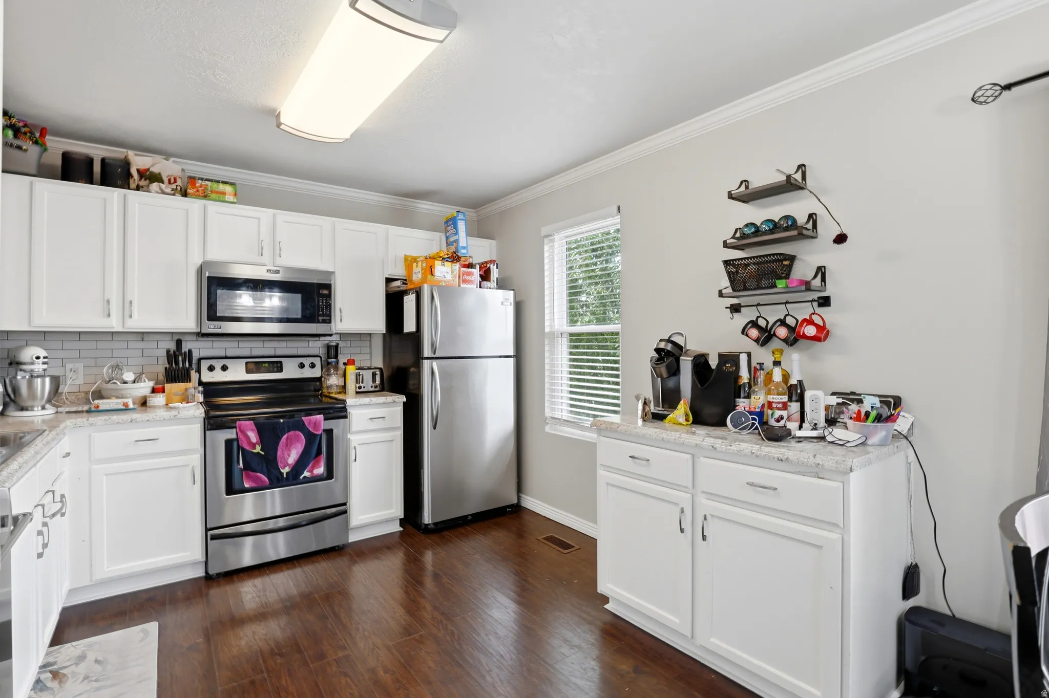 Kitchen featuring white shaker-style cabinetry, stainless steel appliances, a subway tile backsplash, and light-toned countertops