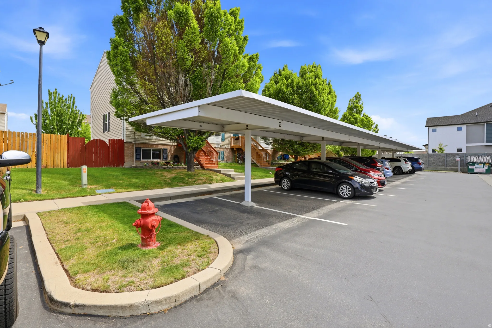 Covered parking structure with multiple spaces, featuring an asphalt surface and a manicured lawn area