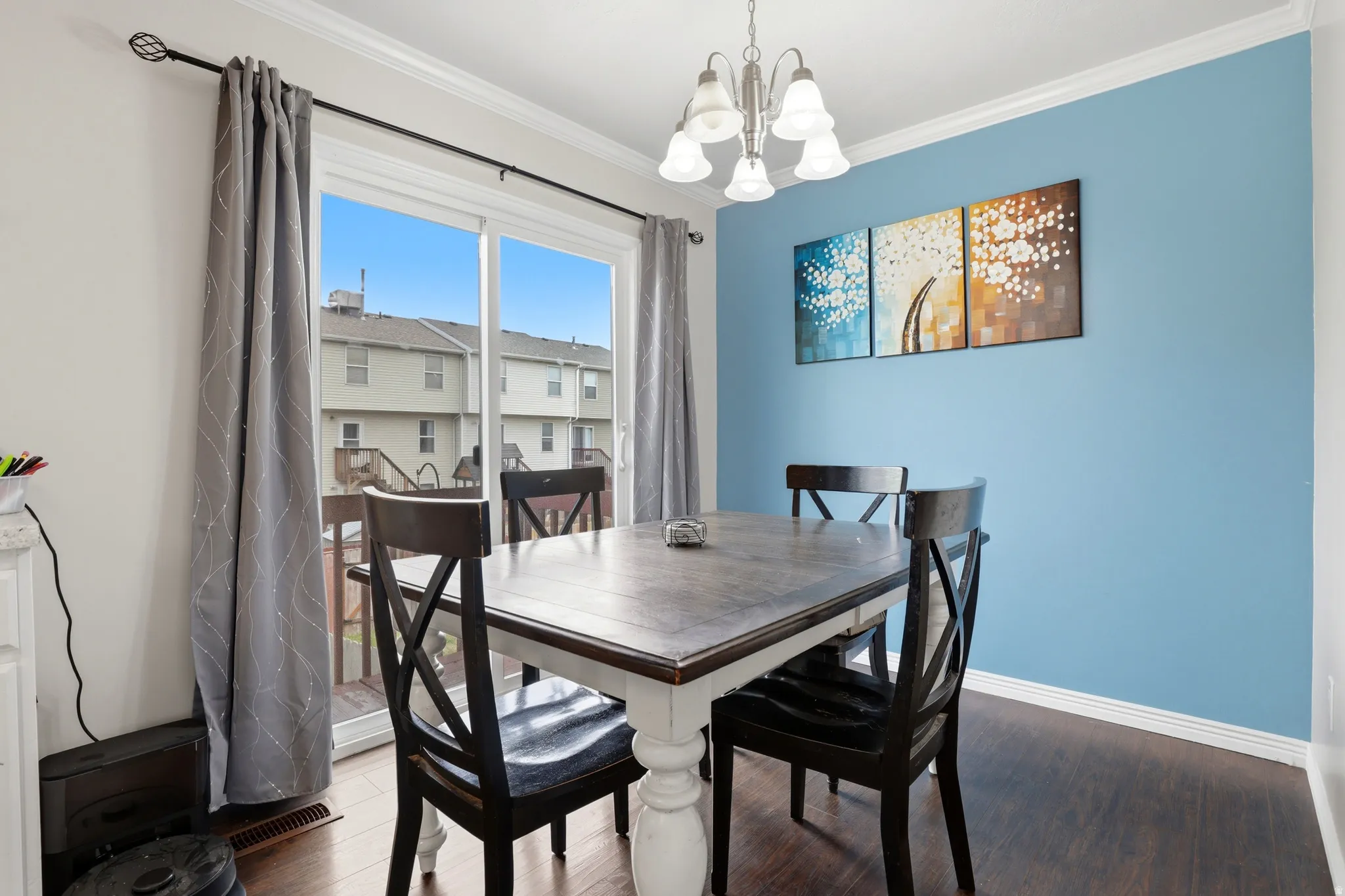 Dining area featuring a sliding glass door, crown molding, a built-in chandelier, dark wood-finish flooring, and a pastel blue accent wall