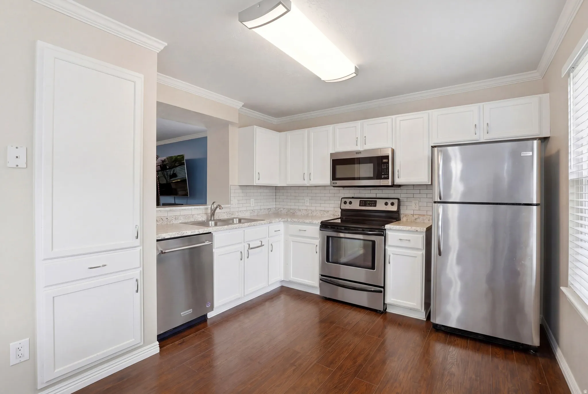 Kitchen featuring white cabinetry, stainless steel appliances, speckled countertops, a subway tile backsplash, and wood-finish flooring