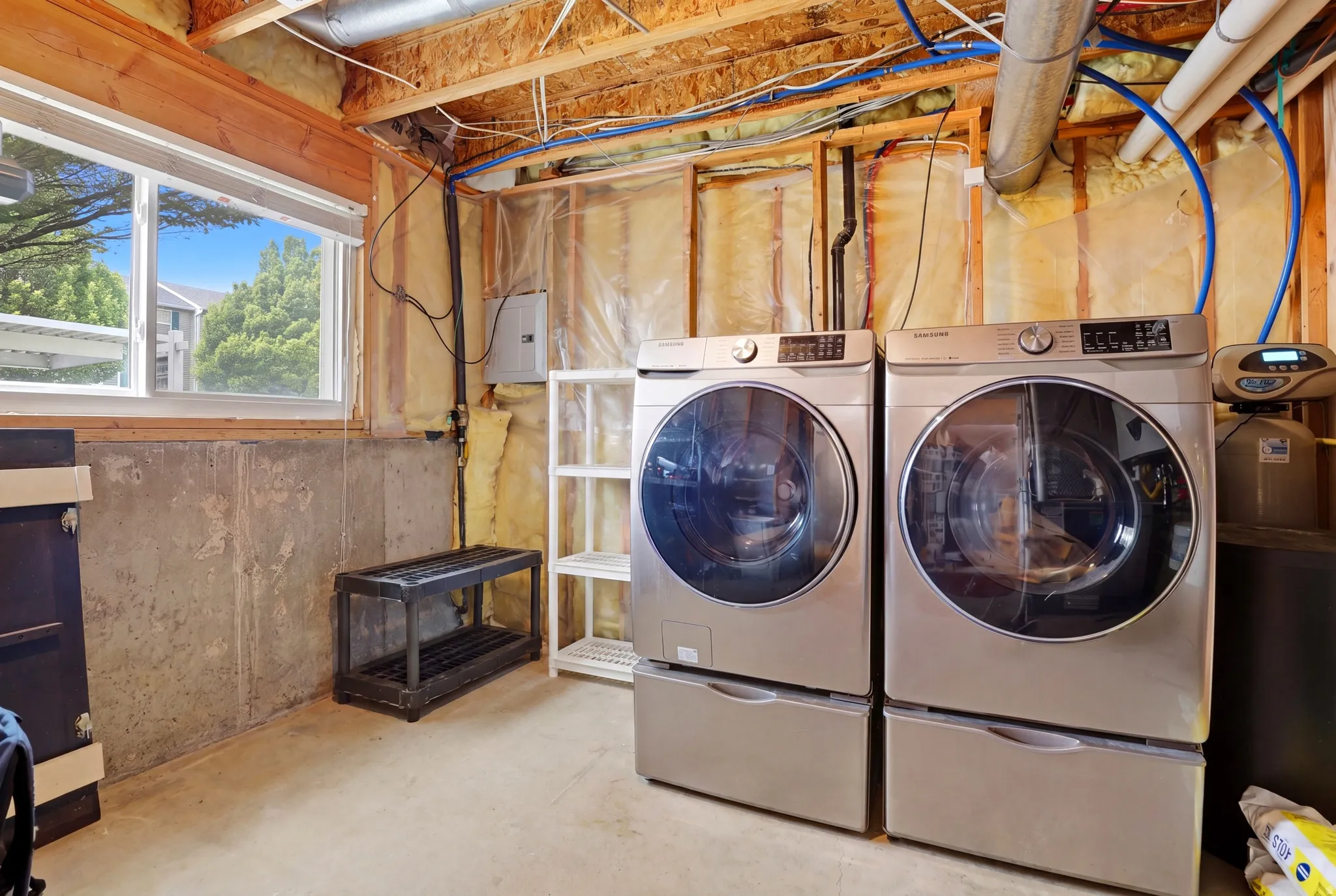 Laundry area with exposed wood framing, concrete foundation walls, and a window