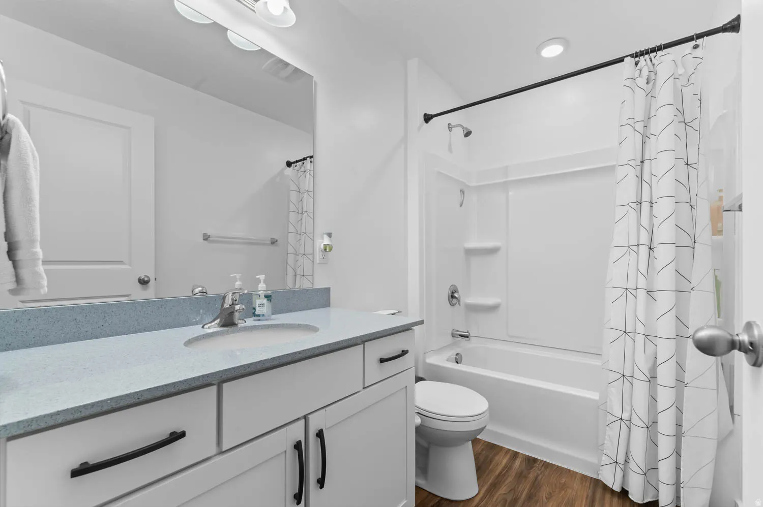 Bright bathroom featuring a single vanity with a light-toned countertop, a built-in sink, and white cabinetry with dark hardware