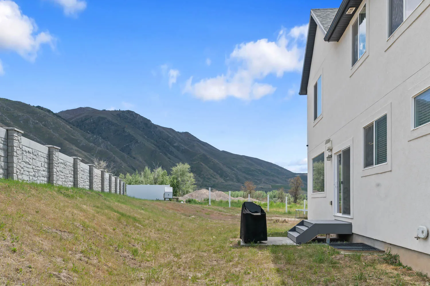 Side exterior of the property featuring a stone block perimeter fence, a concrete patio area, and rear entry steps