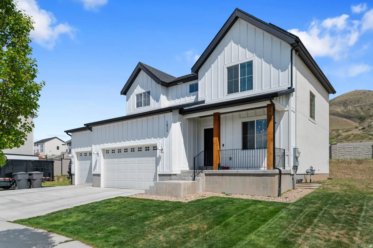 Modern farmhouse-style exterior featuring white board and batten siding, black trim, a covered porch with natural wood columns, a three-car garage, and a manicured front lawn