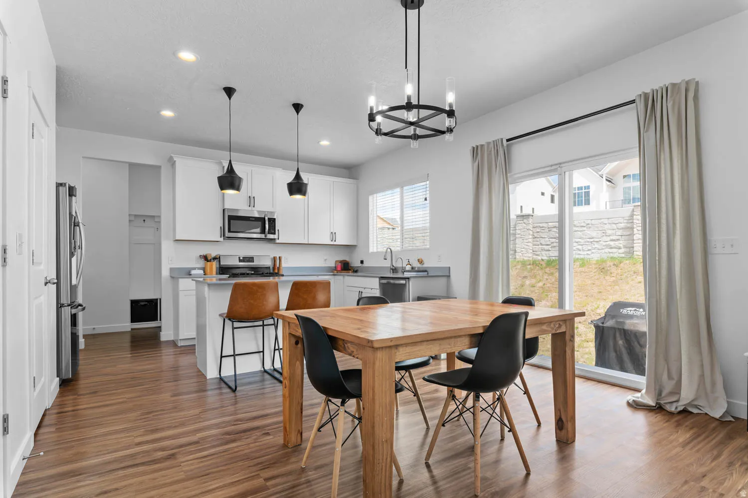 Open-concept kitchen and dining area featuring wood-finish flooring, white cabinetry, stainless steel appliances, and a central island with bar seating