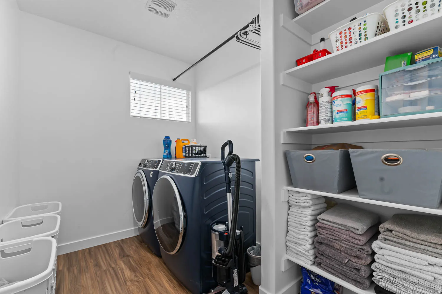 Dedicated laundry space featuring wood-finish flooring, a window with blinds, and built-in shelving