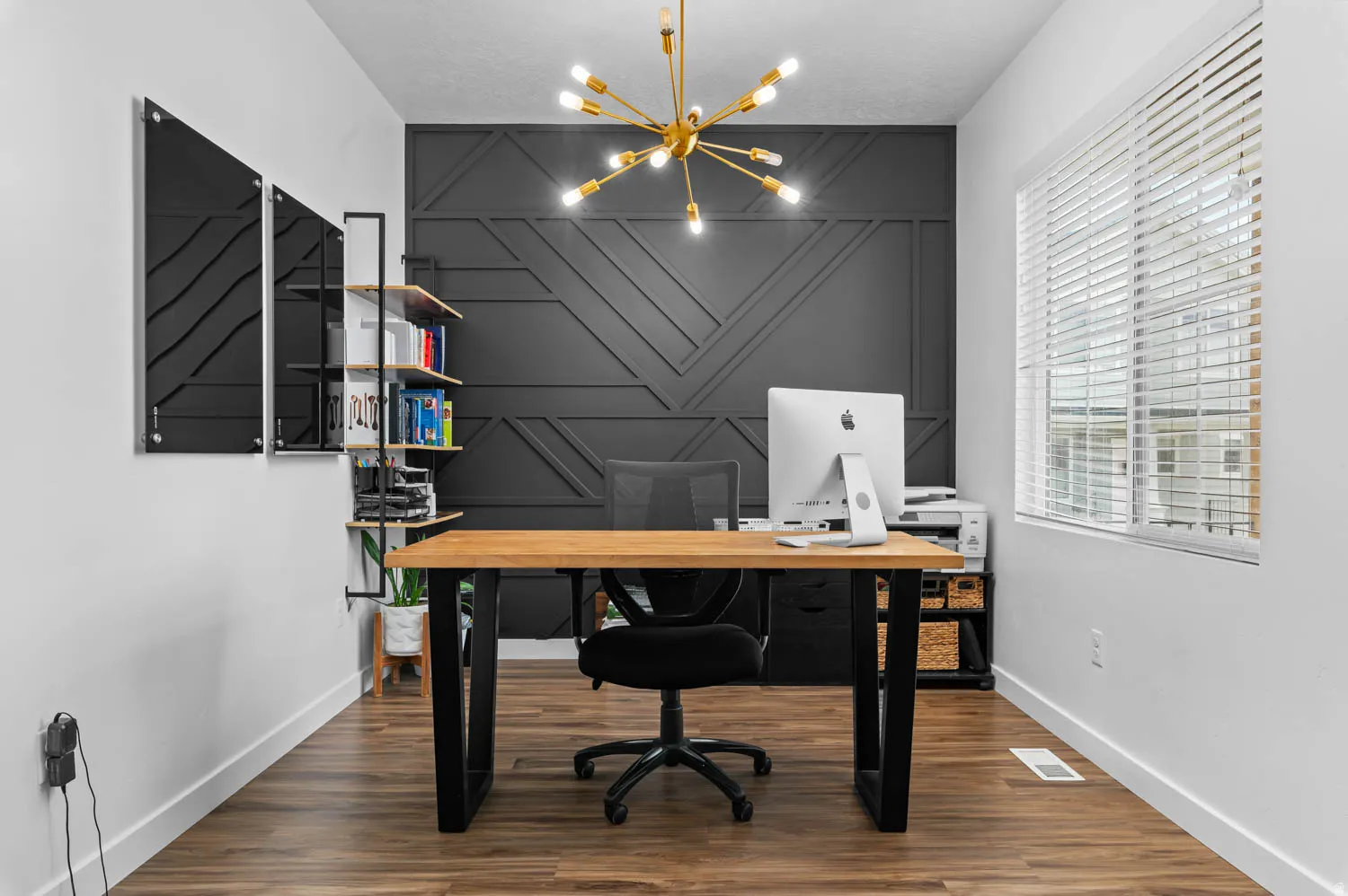 Dedicated workspace featuring an accent wall with geometric paneling, wood-finish flooring, and a modern sputnik chandelier