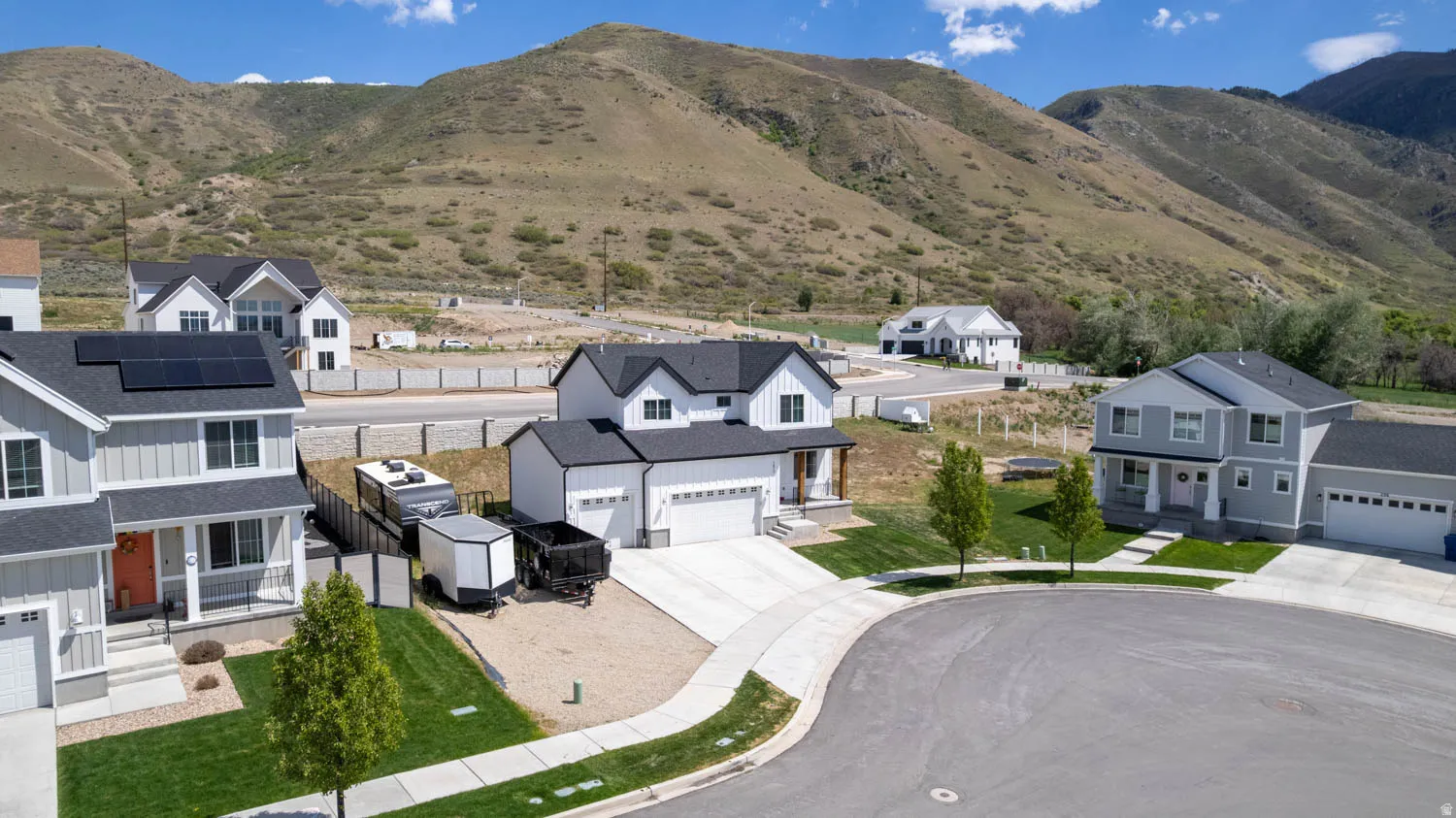 Modern home with a two-car garage, concrete driveway, and a manicured front lawn, set against a mountainous backdrop