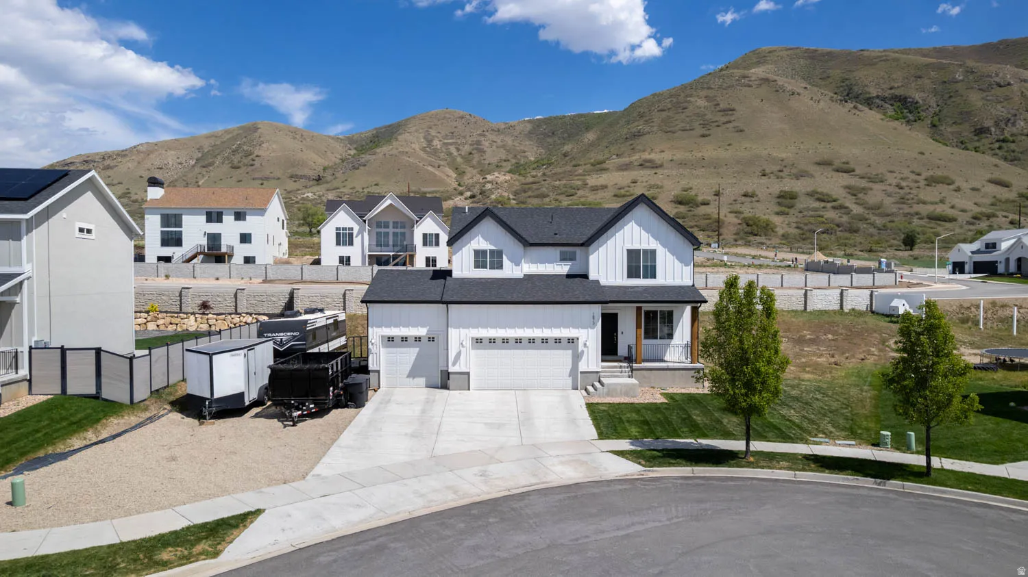 Modern farmhouse exterior featuring white vertical siding, black trim, a two-car garage, and a covered front porch with wood-finish columns