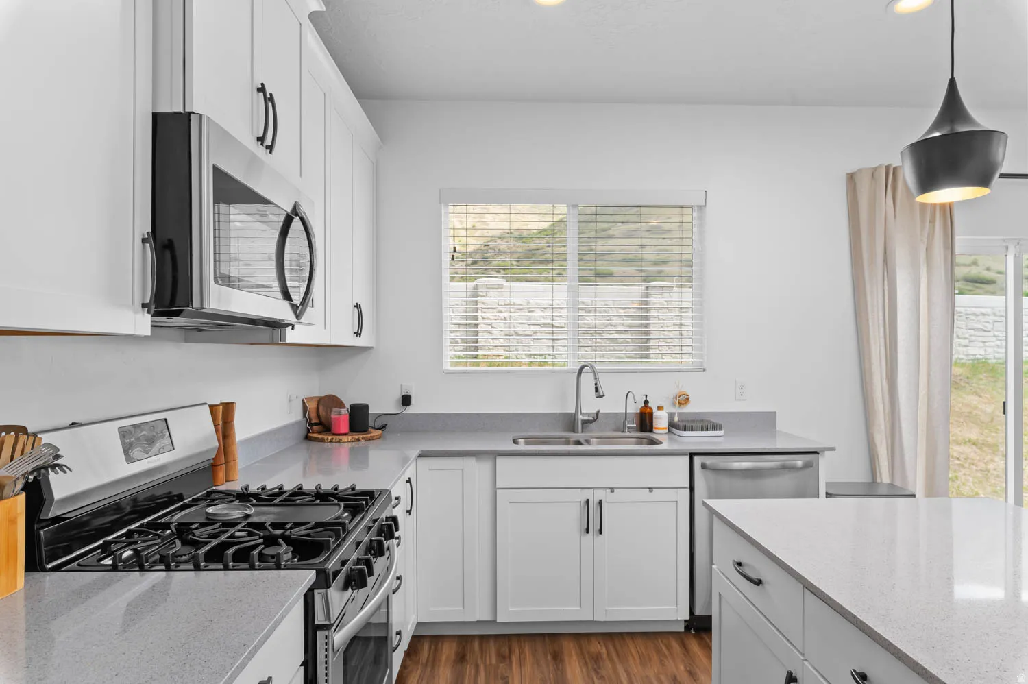 Contemporary kitchen featuring white shaker cabinetry, stainless steel appliances, light-toned countertops, wood-finish flooring, and a sliding glass door