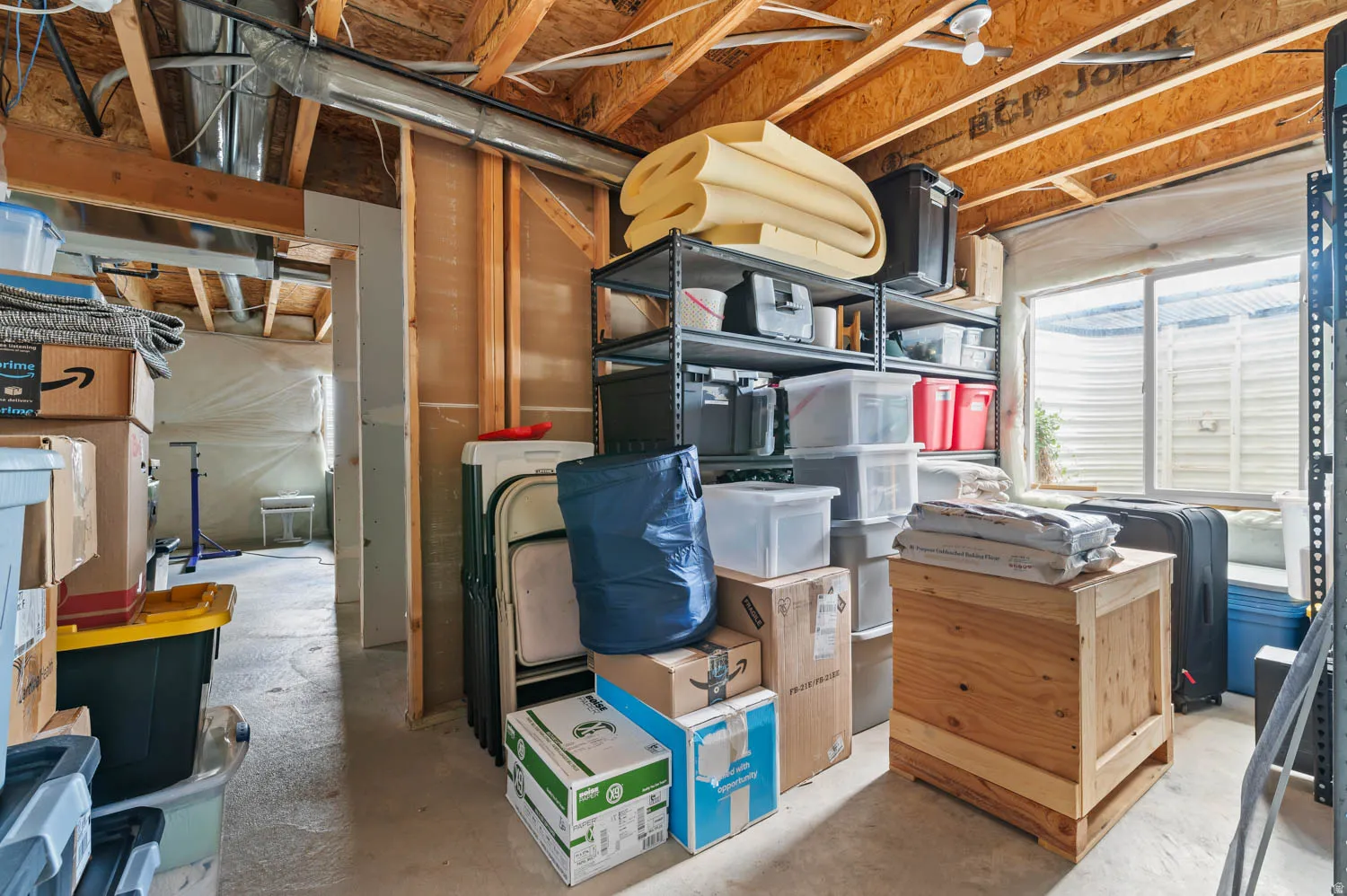 Unfinished basement space featuring exposed wood joists, structural framing, and a window well
