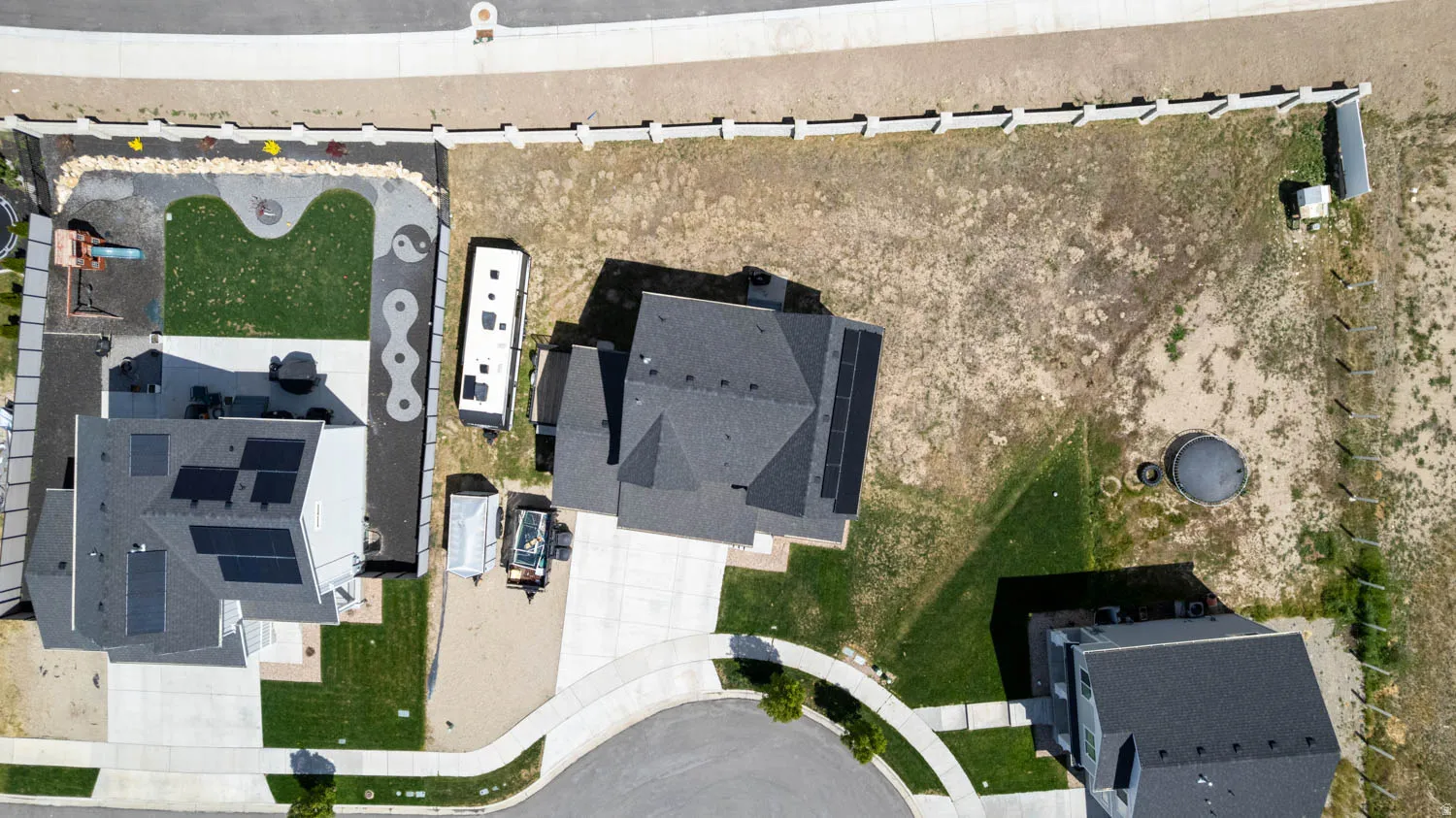 Expansive property featuring a contemporary residence with solar panel installation, a concrete driveway, and an established lawn area with a paved patio