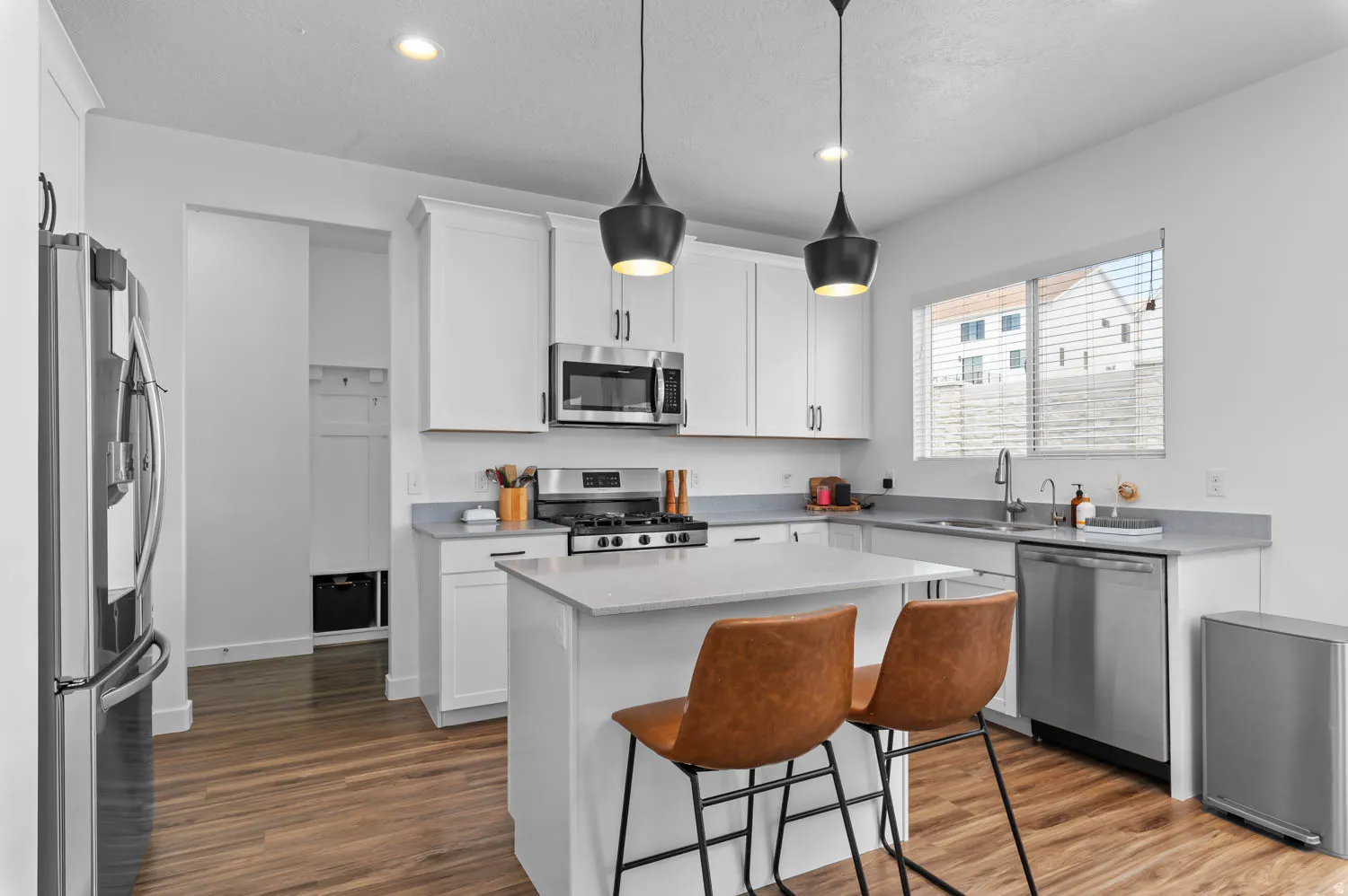 Modern kitchen featuring white shaker cabinetry, stainless steel appliances, a center island with seating, pendant lighting, and wood-finish flooring