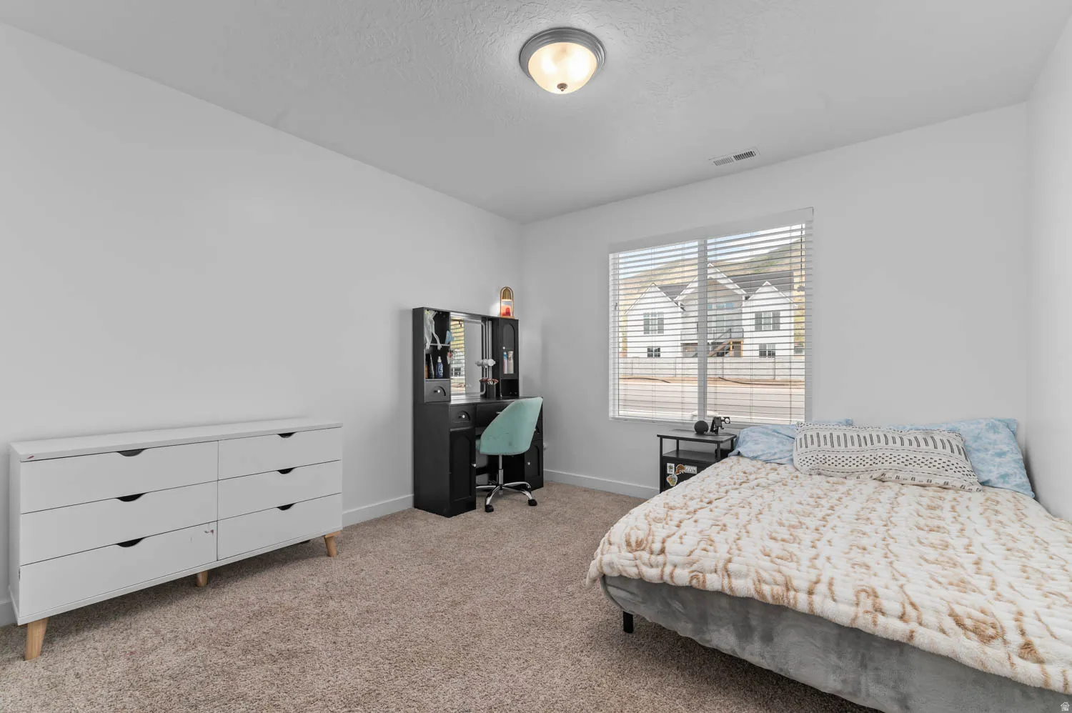 Bright bedroom featuring a large window with horizontal blinds, neutral wall paint, and plush carpet flooring