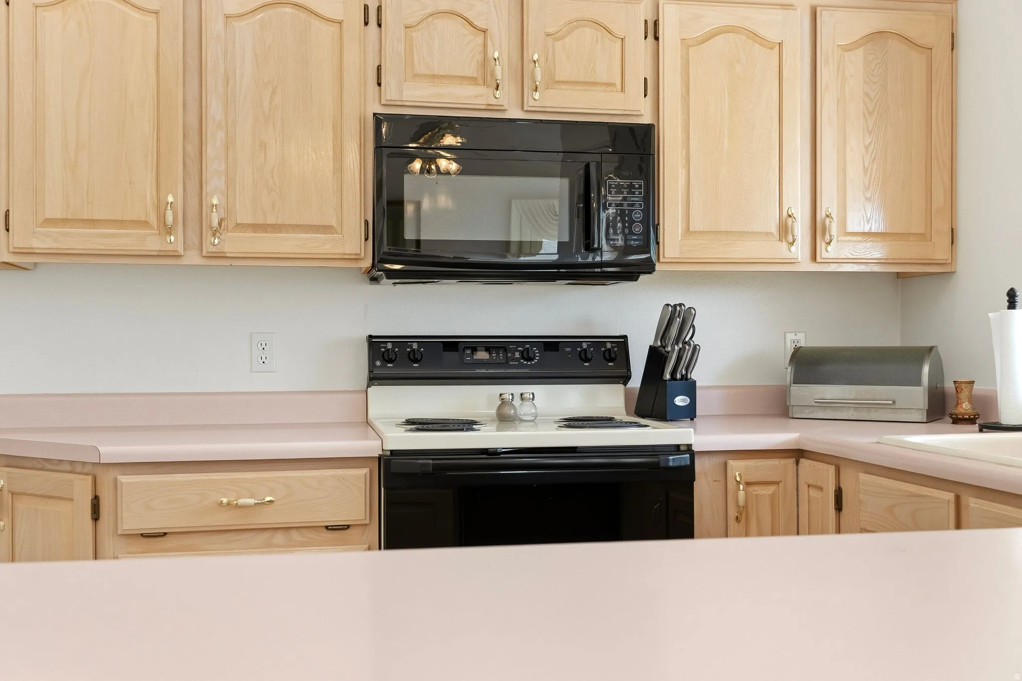 Kitchen featuring light wood cabinetry with arched top panels, a built-in microwave, and solid surface countertops