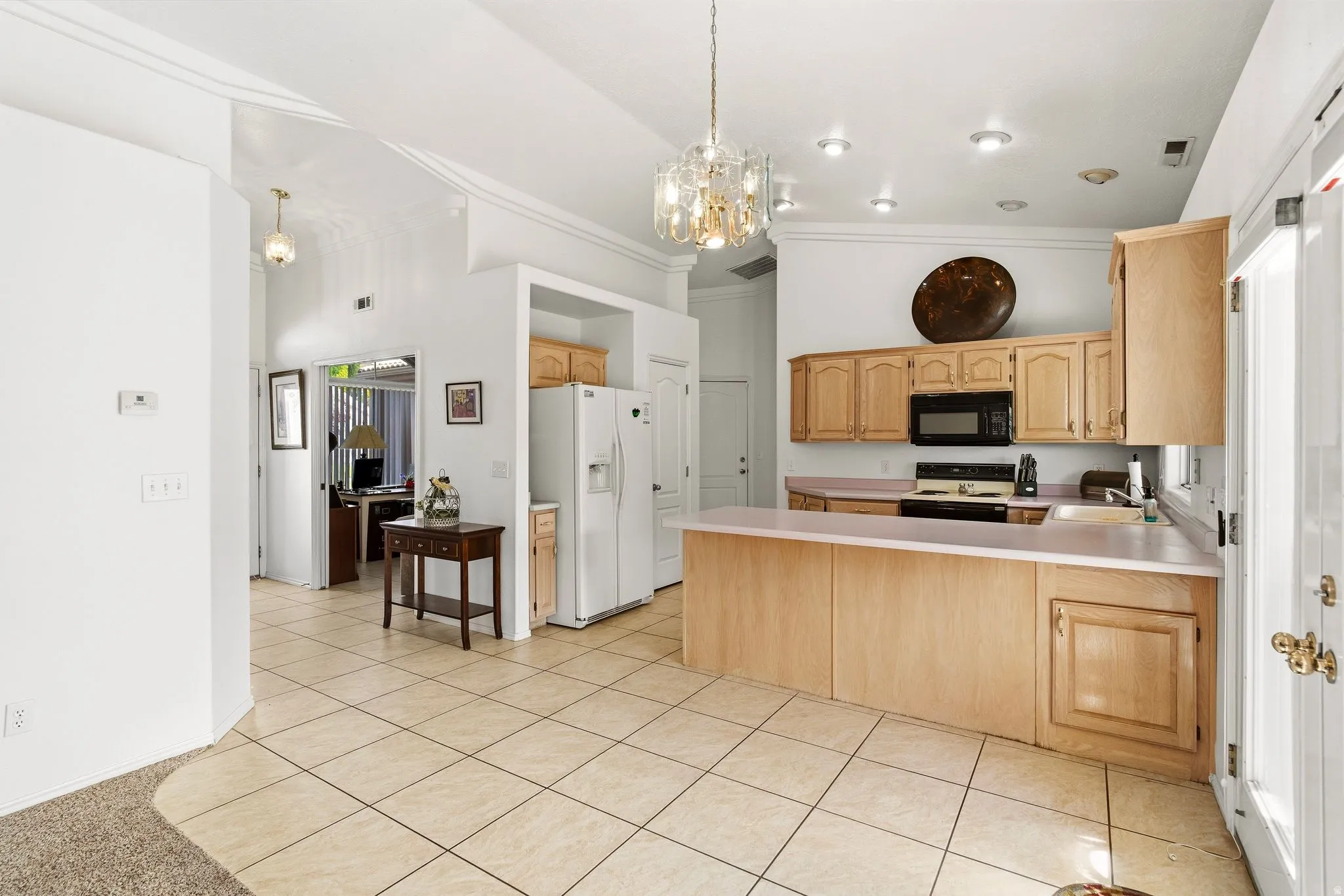 Kitchen featuring light wood-finish cabinetry, tile flooring, and integrated black appliances