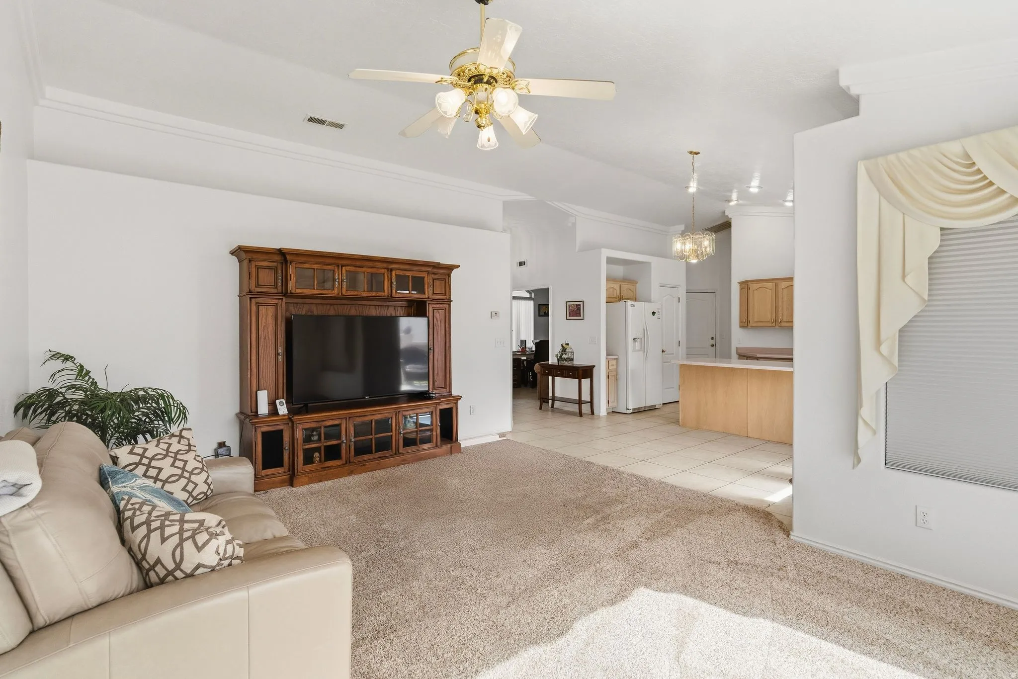Expansive room featuring vaulted ceilings, crown molding, a ceiling fan with light fixture, carpeted flooring, and tile flooring in the background