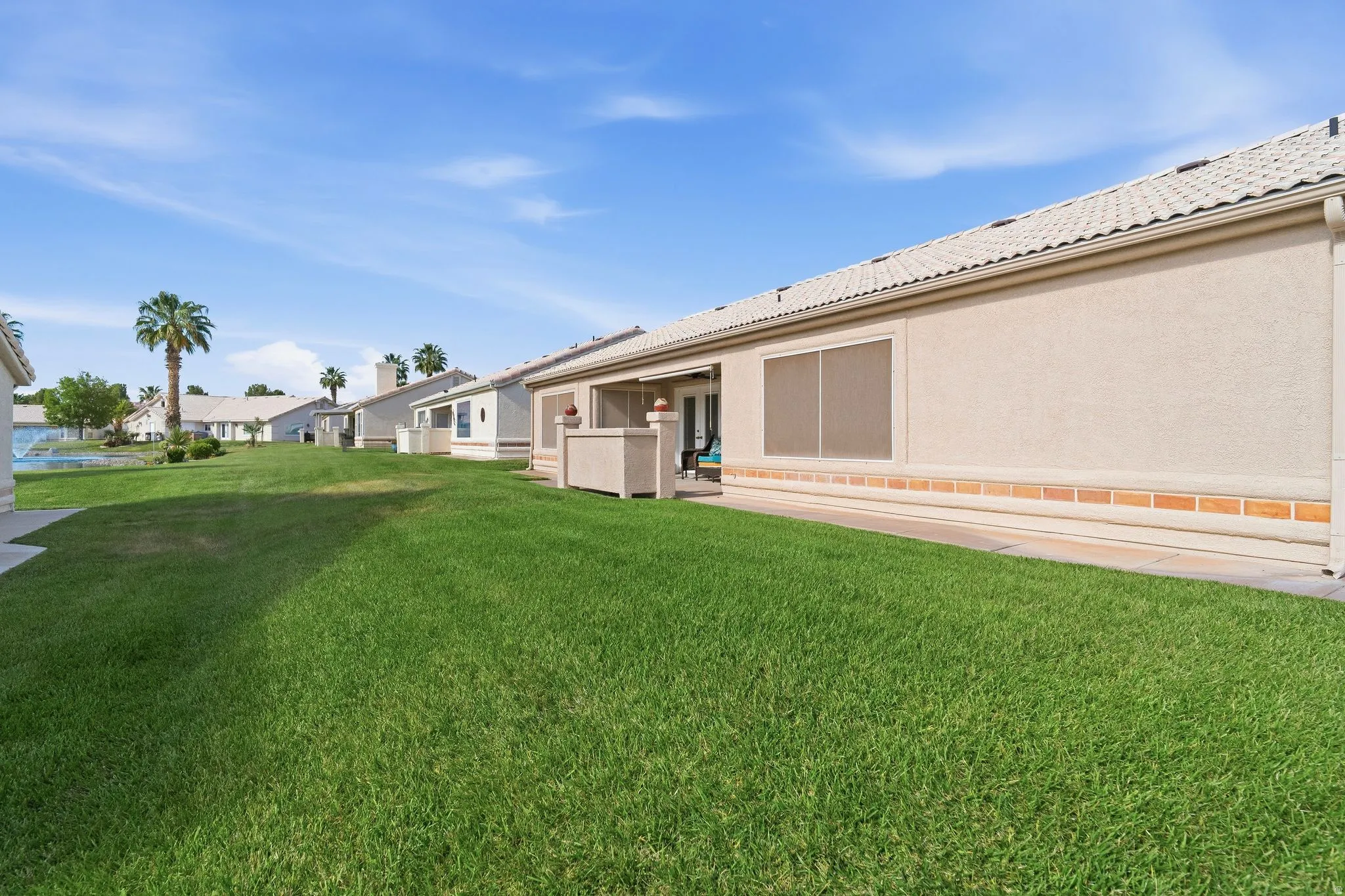 Expansive green space featuring a stucco exterior with a brick-finish base, tiled roof, and screened patio area