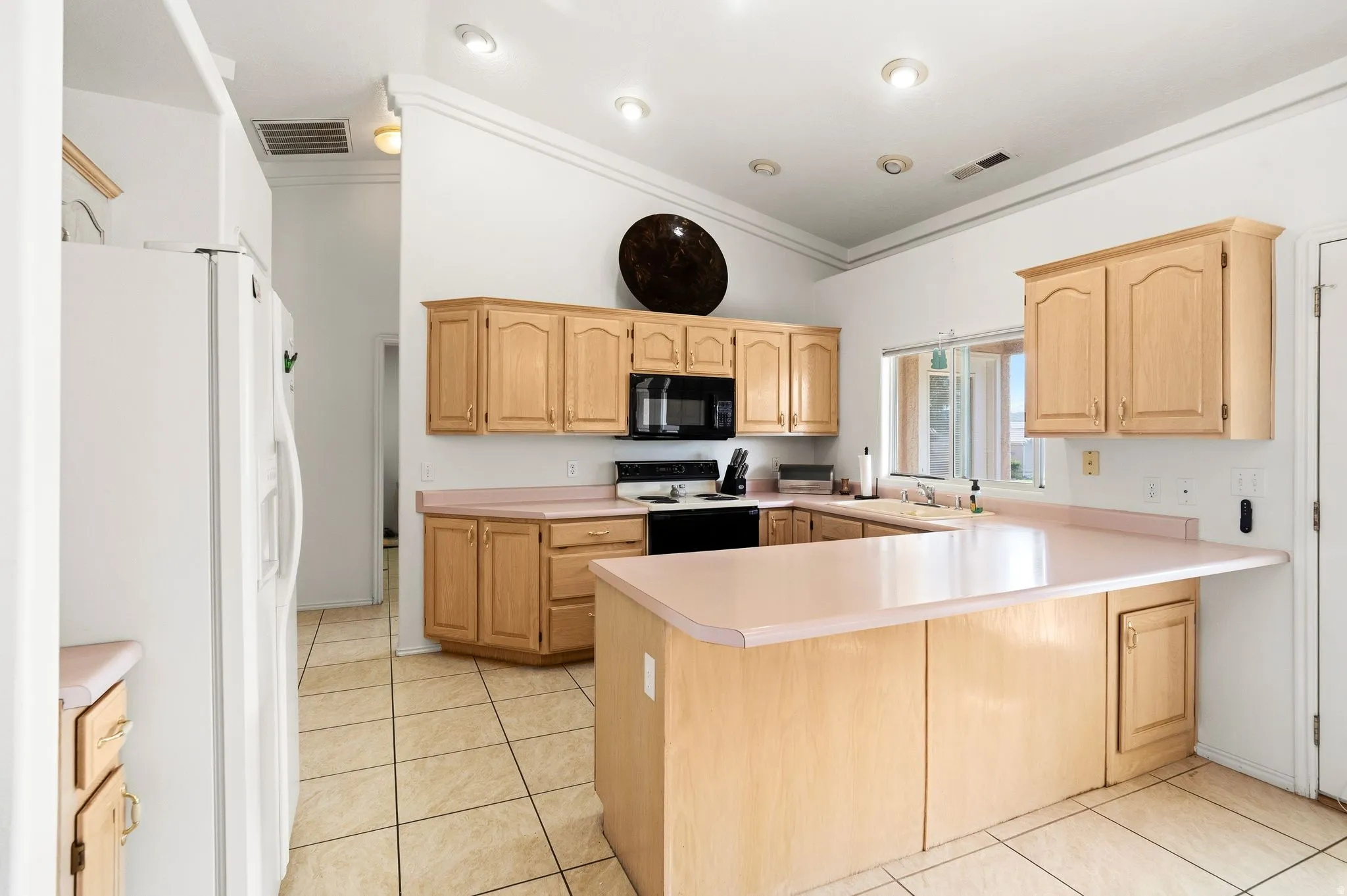 Expansive kitchen featuring light wood cabinetry, a built-in black oven and microwave, and a large central island with countertop seating