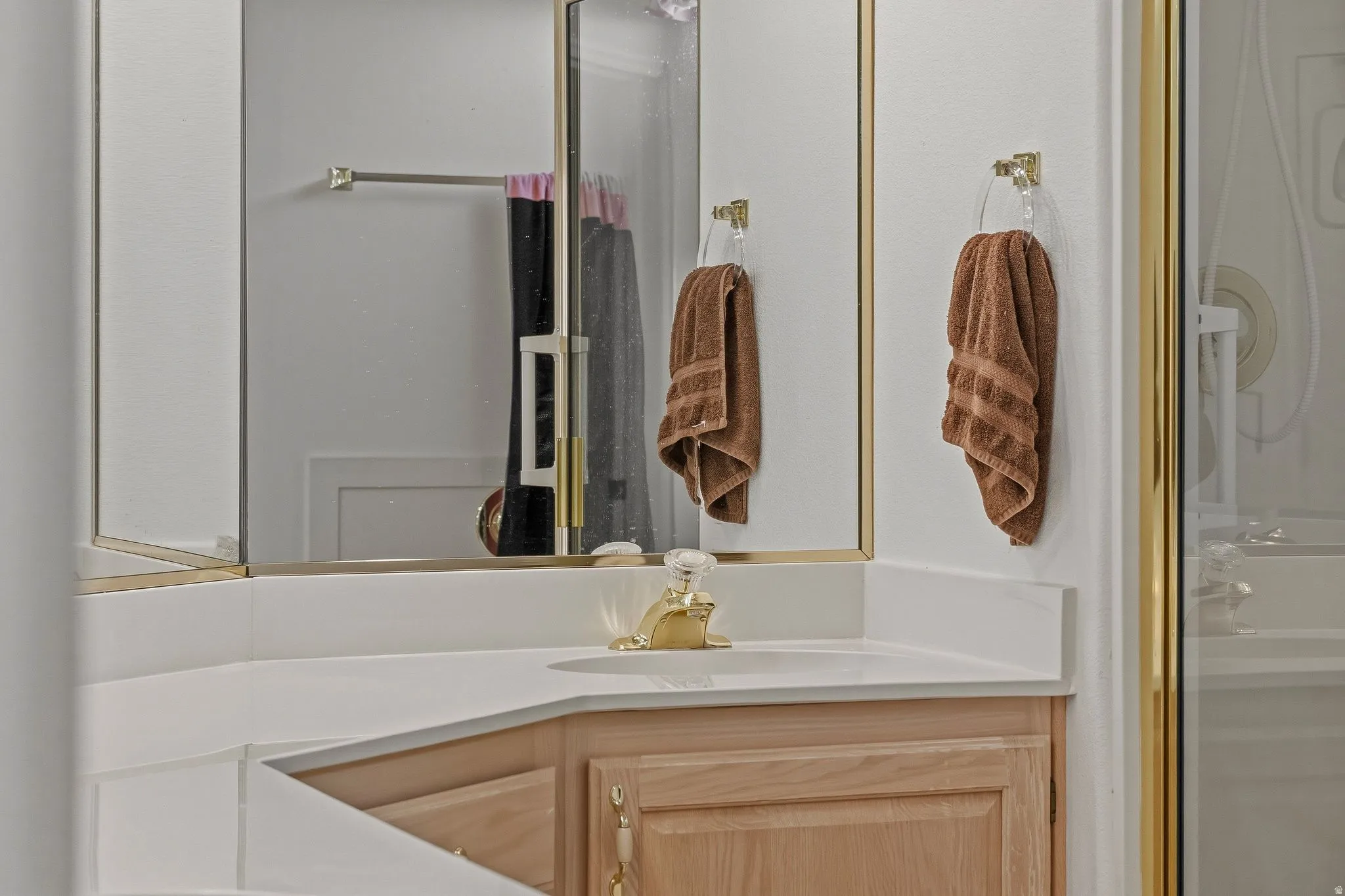 Bathroom vanity featuring a corner sink, light wood cabinetry, white countertop, and gold-finish fixtures