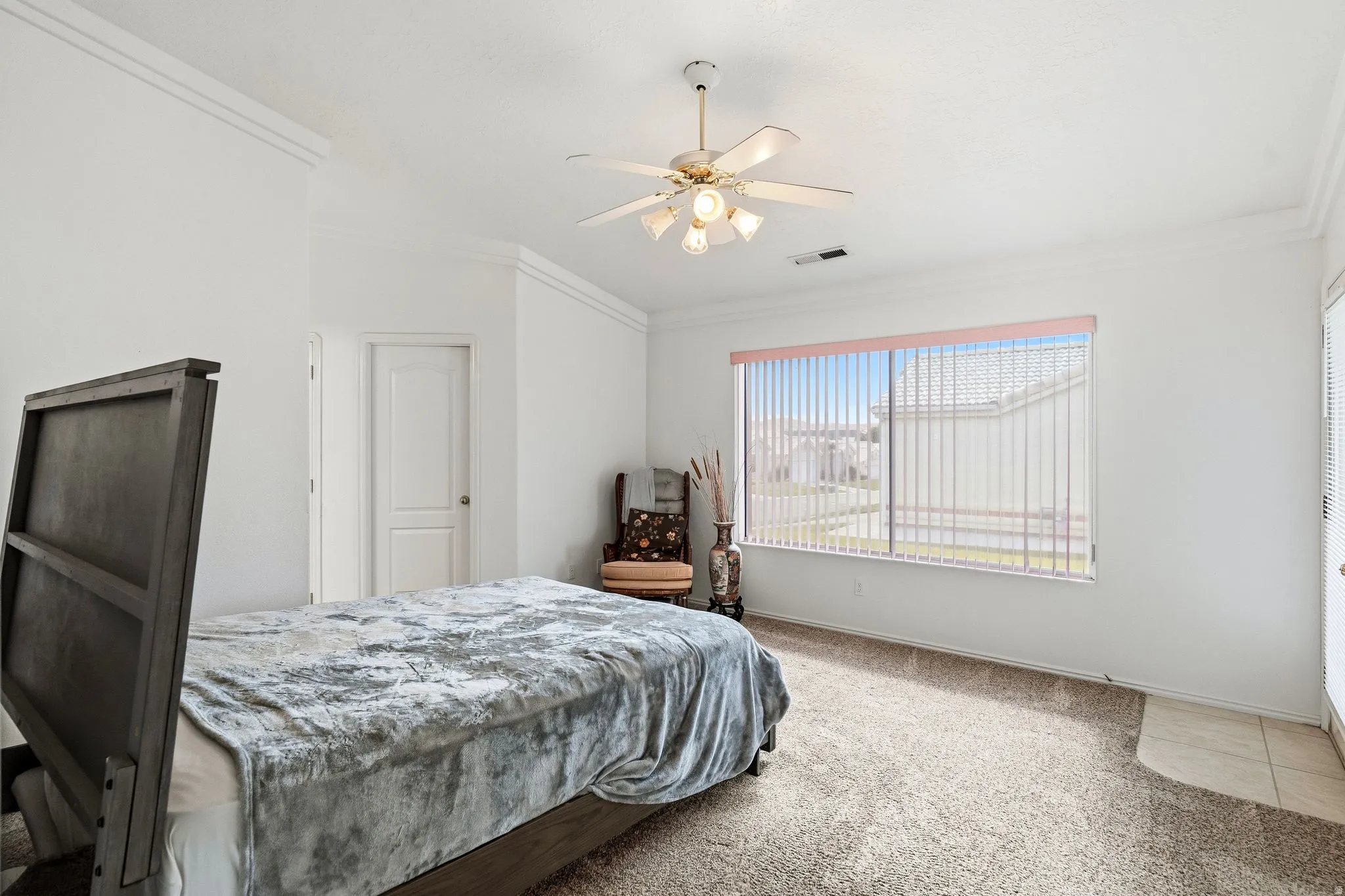 Bright interior space featuring a large window with vertical blinds, crown molding, a ceiling fan with integrated lighting, and carpeted flooring