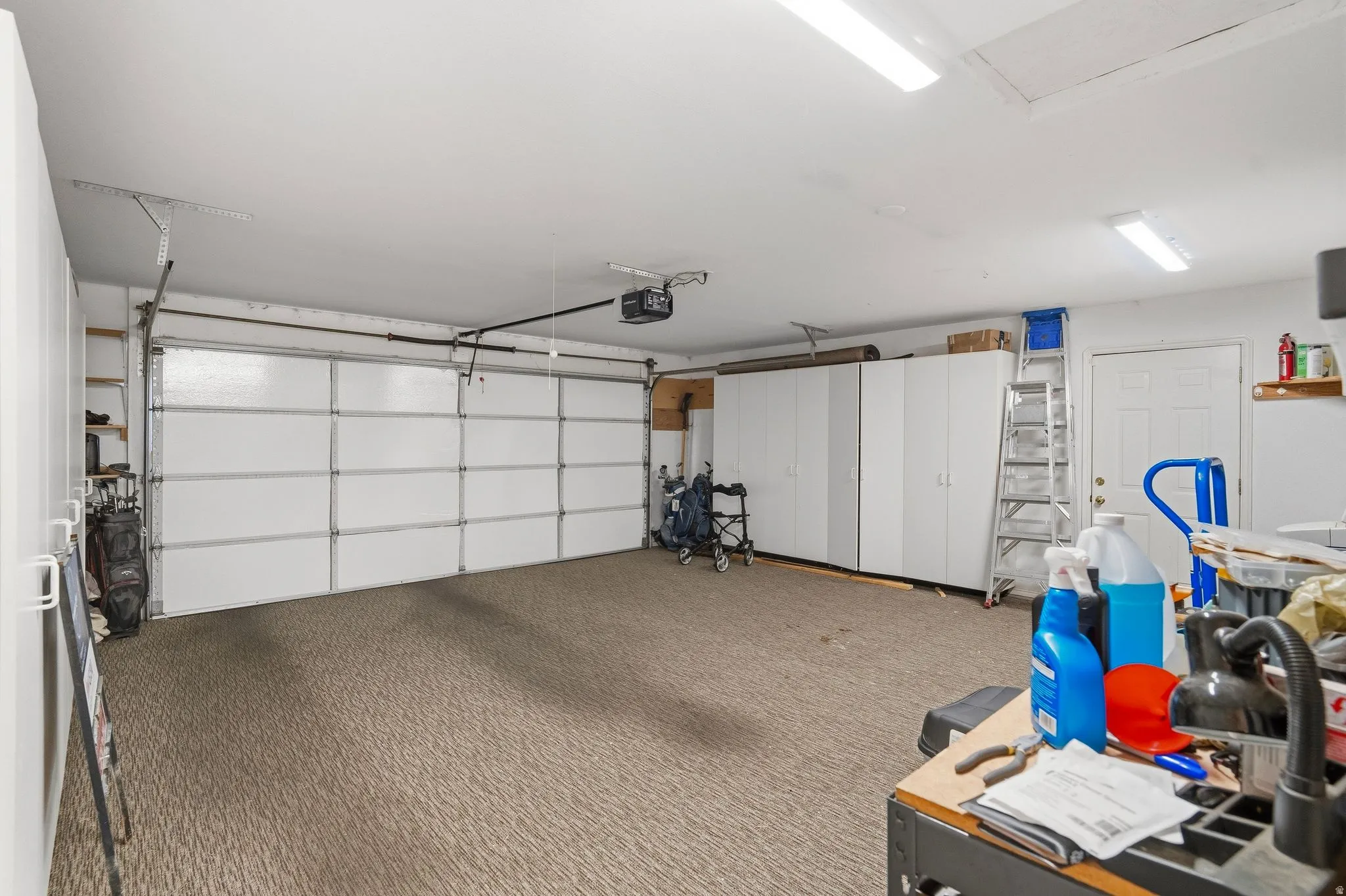 Spacious garage featuring a paneled overhead door, built-in white cabinetry, textured flooring, and fluorescent ceiling lighting