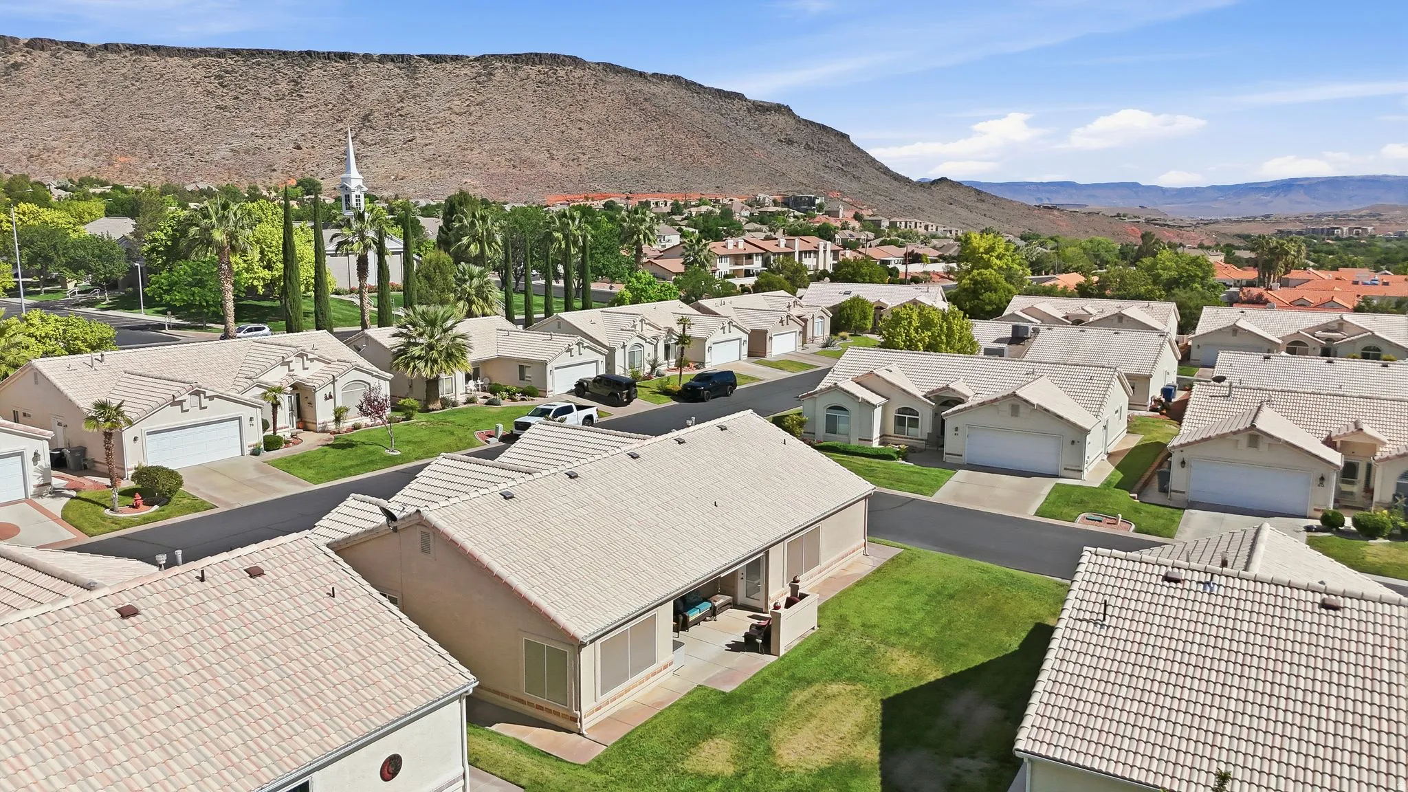 Residential community featuring single-story homes with attached garages, light-colored tile roofs, and manicured green lawns